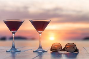 Two glasses of red wine with sunglasses and a sunset in the background
