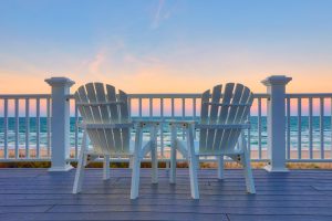 Two Adirondack chairs on a balcony facing the ocean